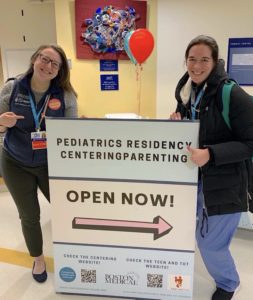 A few members of the Boston Combined Residency Program team join together to innovate a Centering Program in an Adolescent Clinic at Boston Medical Center. The two team members hold a sign directing patients to the clinic.