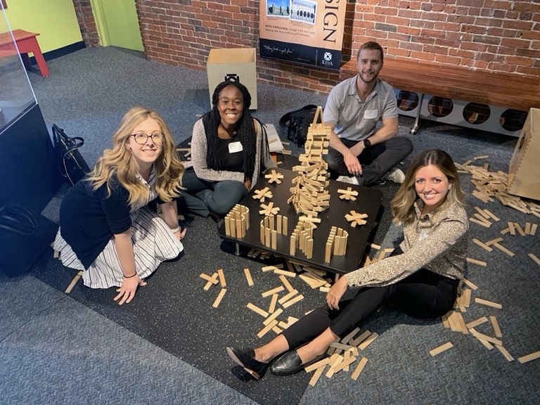 Four interns practicing milestones together using Jenga sticks while sitting on the floor. The residents are smiling with one another as they enjoy themselves.