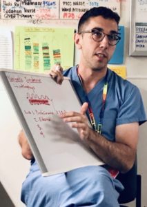 A resident sitting down teaching other team members off a white board, educating to drive the best care possible and lead by example.